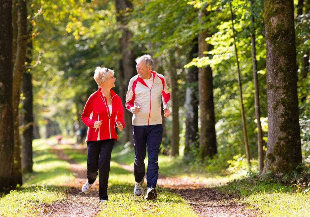 Two older people walking on a path in the woods.