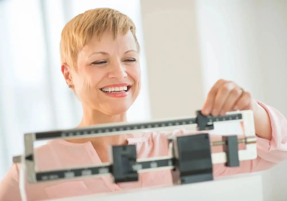 A woman smiles while standing on a scale.