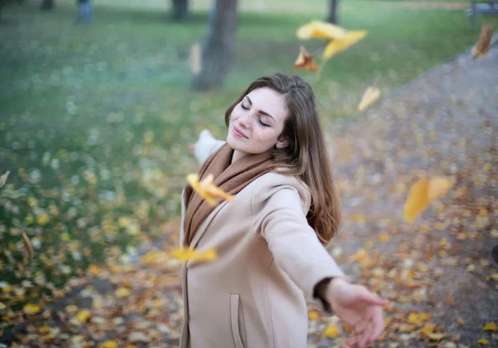 A woman in the park throwing leaves into the air.